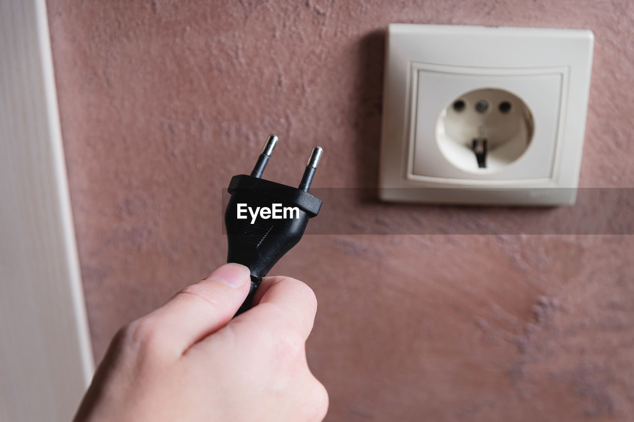 A woman's hand inserts an electric plug into a socket, close-up