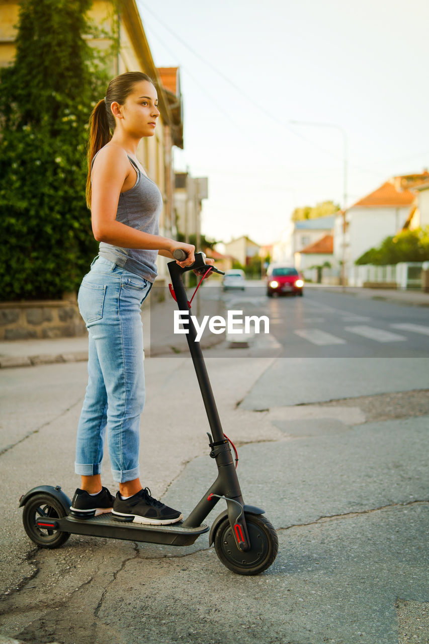 Young woman standing on electric push scooter on street