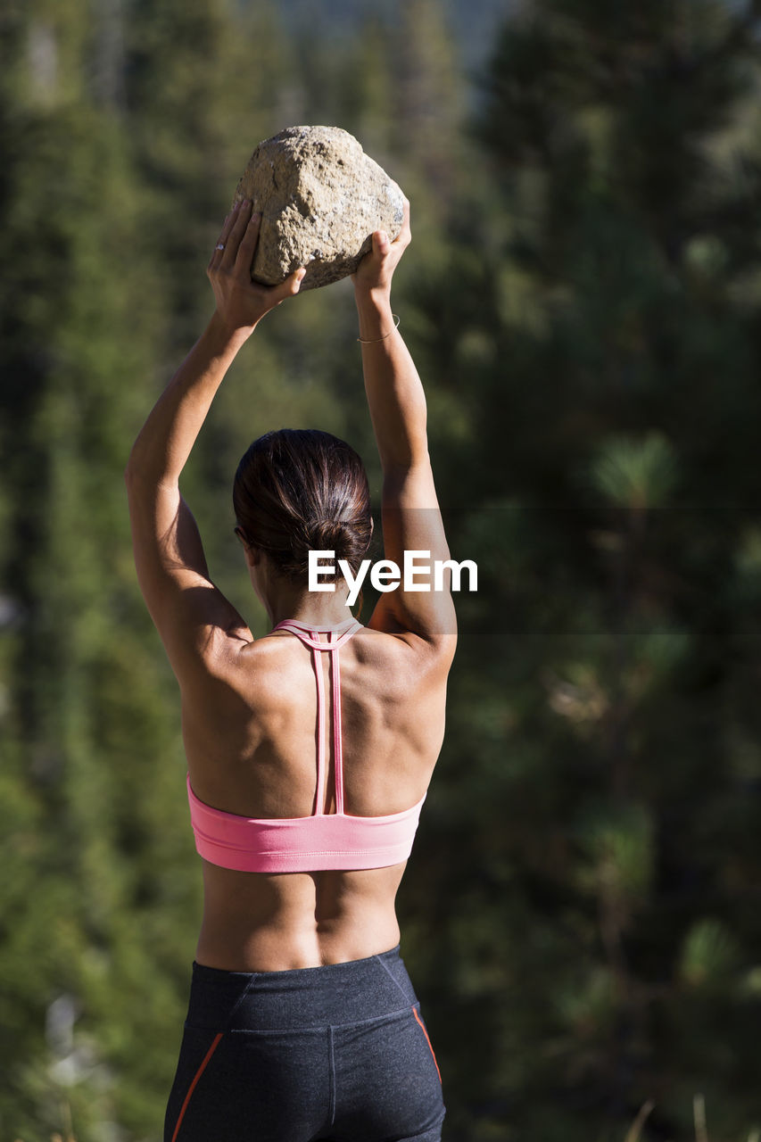 Rear view of athlete picking up stone while exercising on sunny day