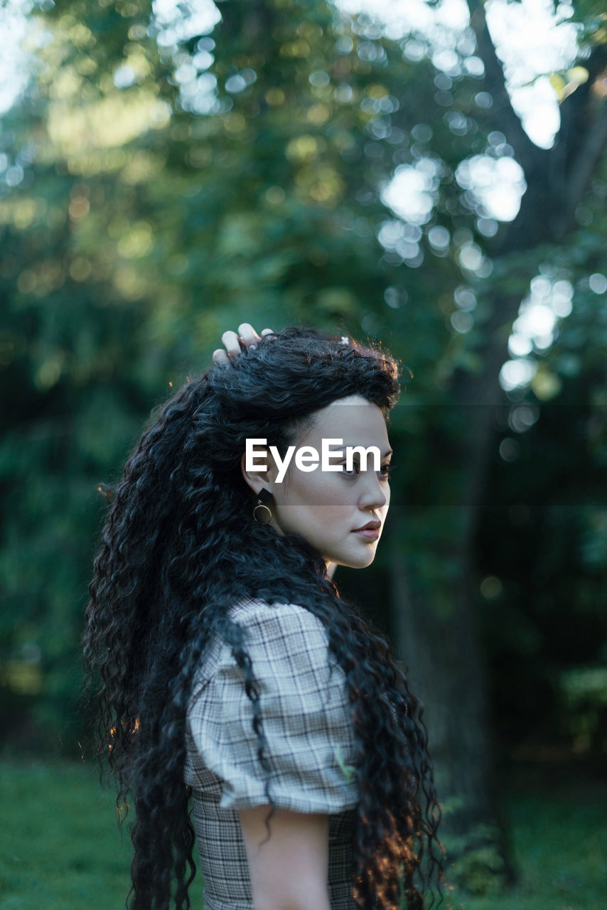 Portrait of young woman looking at tree in forest