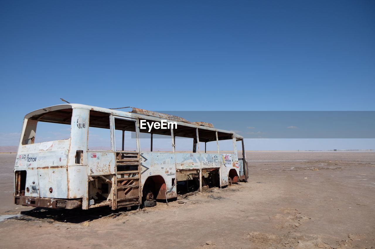 Old damaged bus on field against clear blue sky