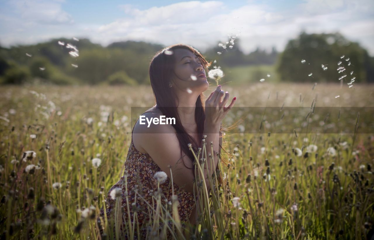 Teenage girl with eyes closed blowing dandelion on land