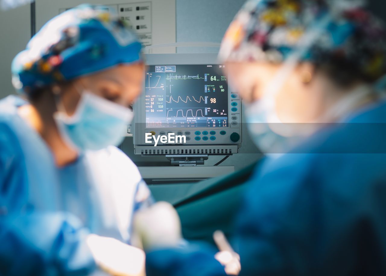 Modern monitor showing vital signs of patient while surgeon and assistant performing operation in modern hospital