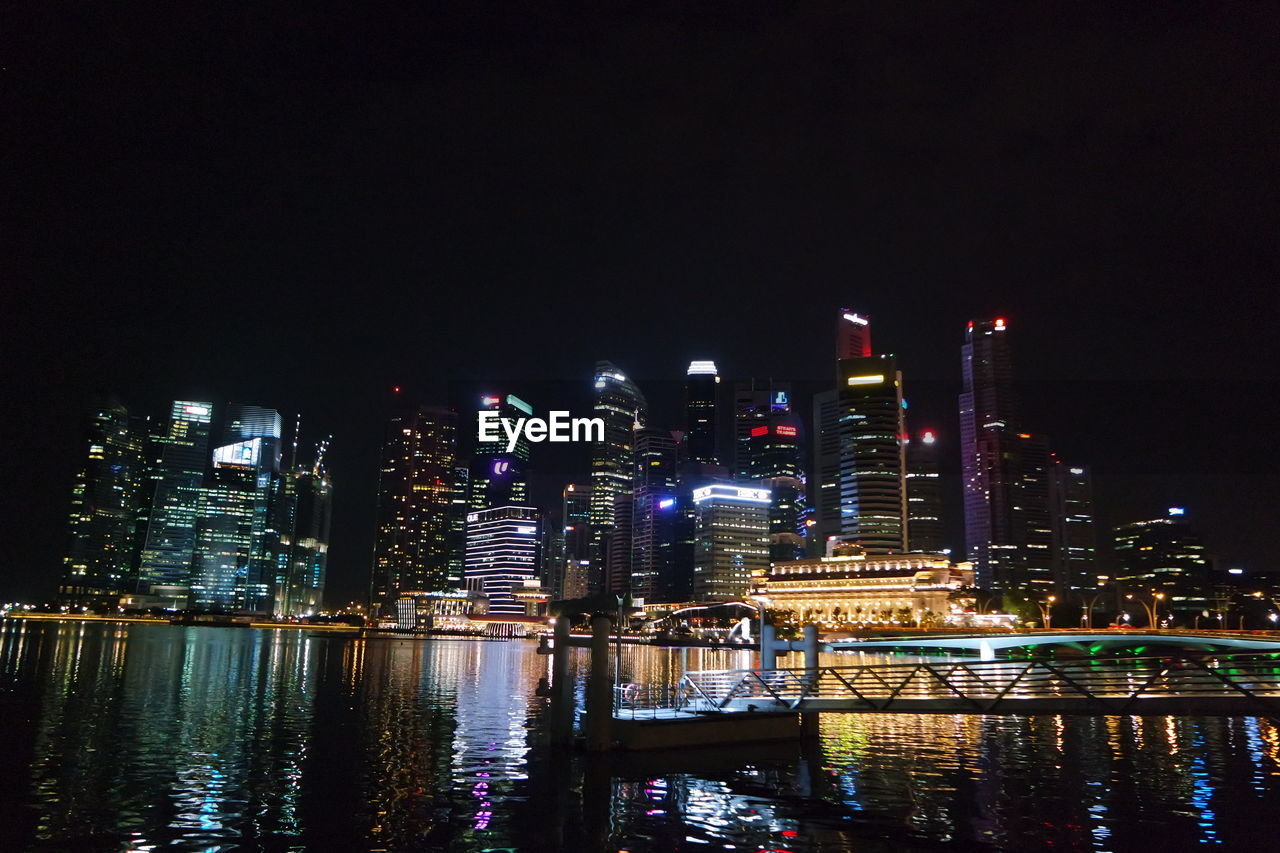 Pier over sea against illuminated buildings in city