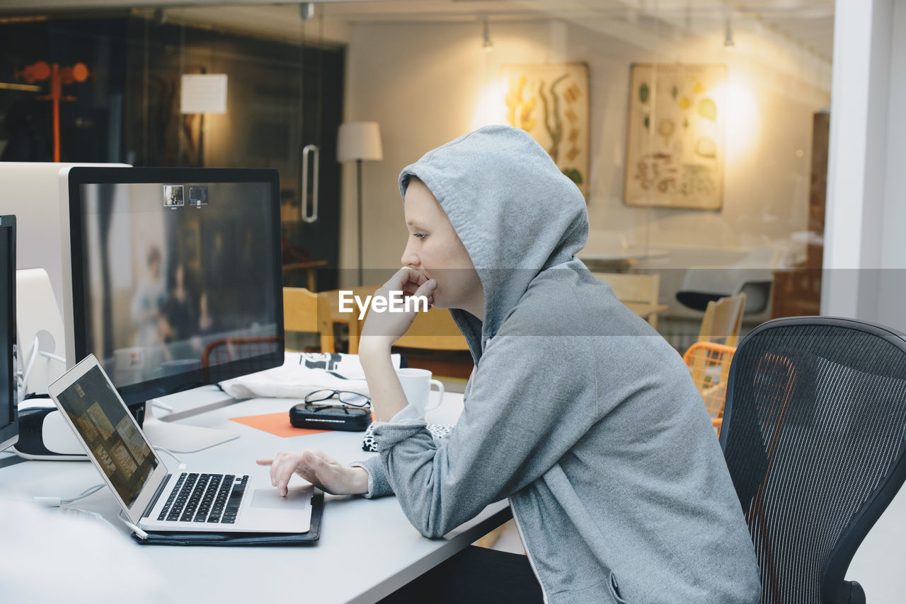 Side view of computer programmer using laptop at desk in office