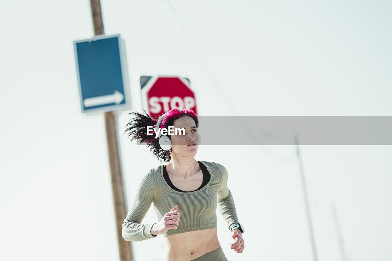 Woman with headphones looking away while running against sign board