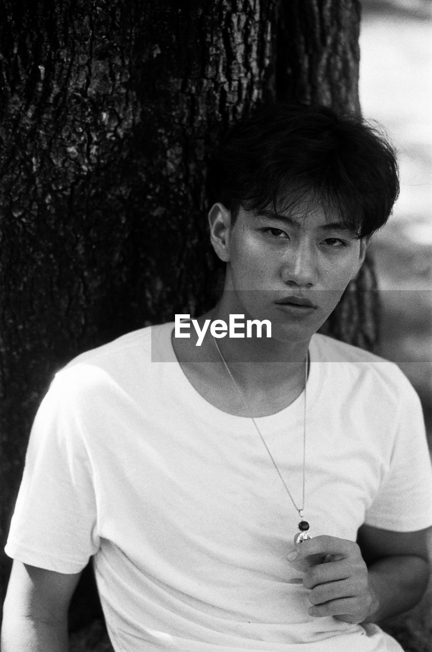 Portrait of young man leaning against tree trunk