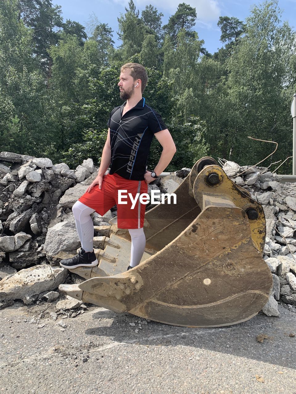 Full length of man wearing shorts standing on metallic bucket outdoors