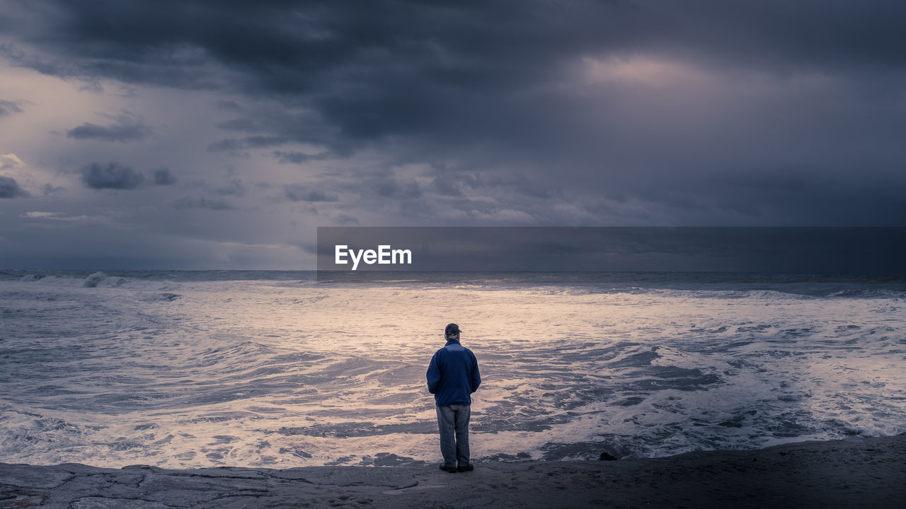 REAR VIEW OF BOY STANDING AT BEACH