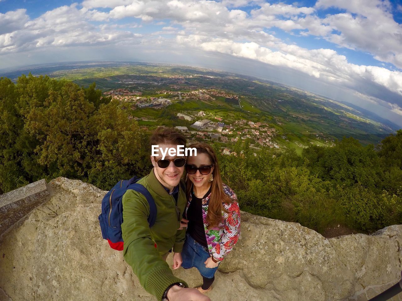 Portrait of smiling young couple standing on mountain peak against landscape