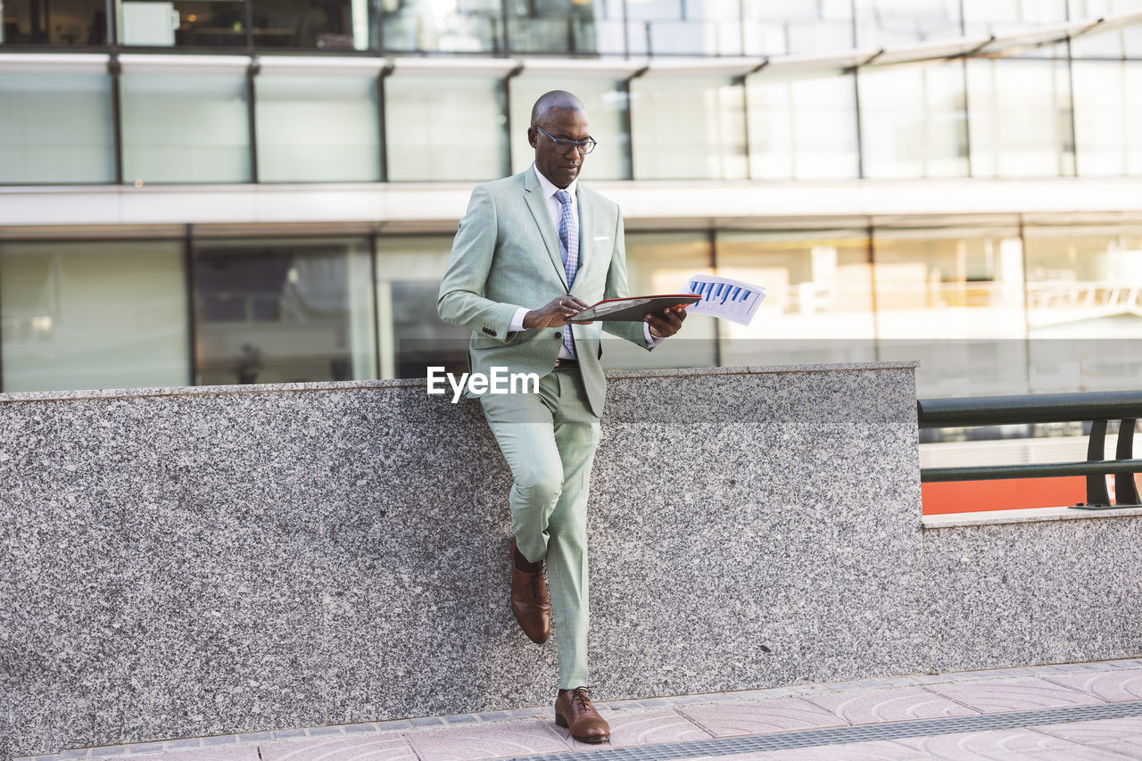 Mature businessman with documents leaning on wall