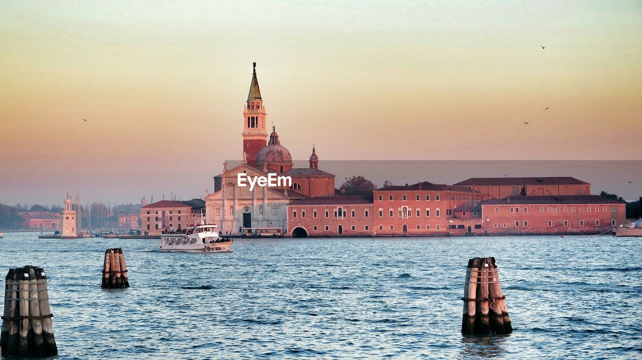 Buildings by sea against sky at sunset