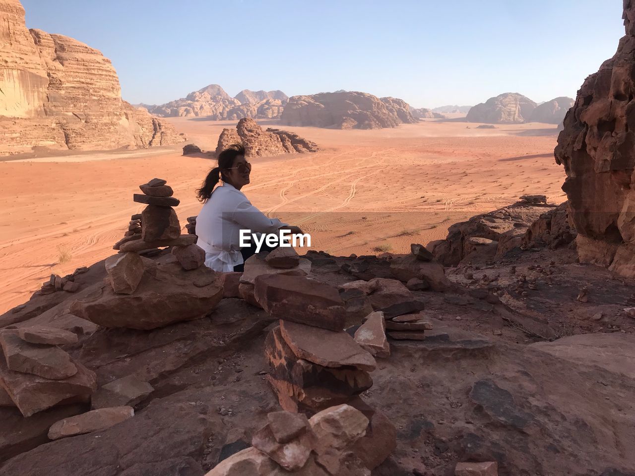 Woman sitting on rock against sky