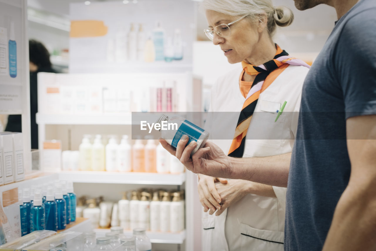 Midsection of male customer checking medicine bottle by female pharmacy store owner