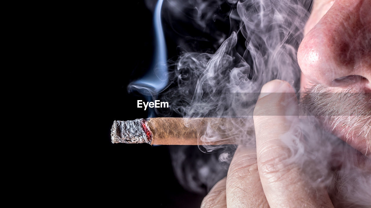 Man smoking cigar against black background