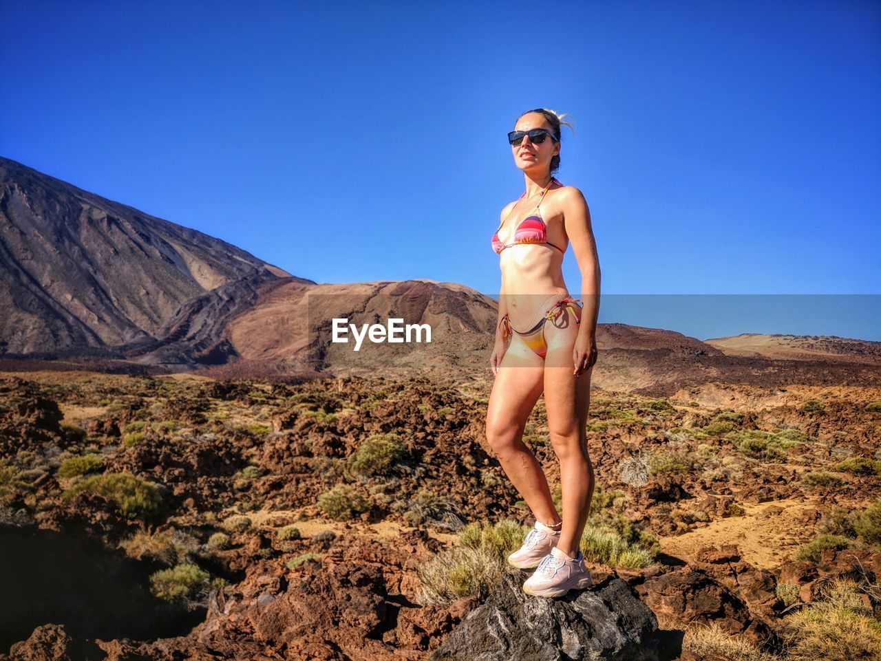 Woman wearing sunglasses while standing on rock against sky