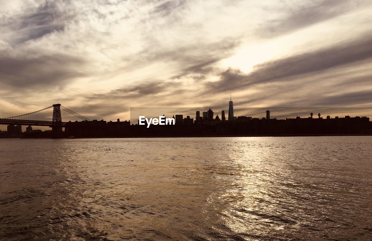 Silhouette of bridge over river against buildings