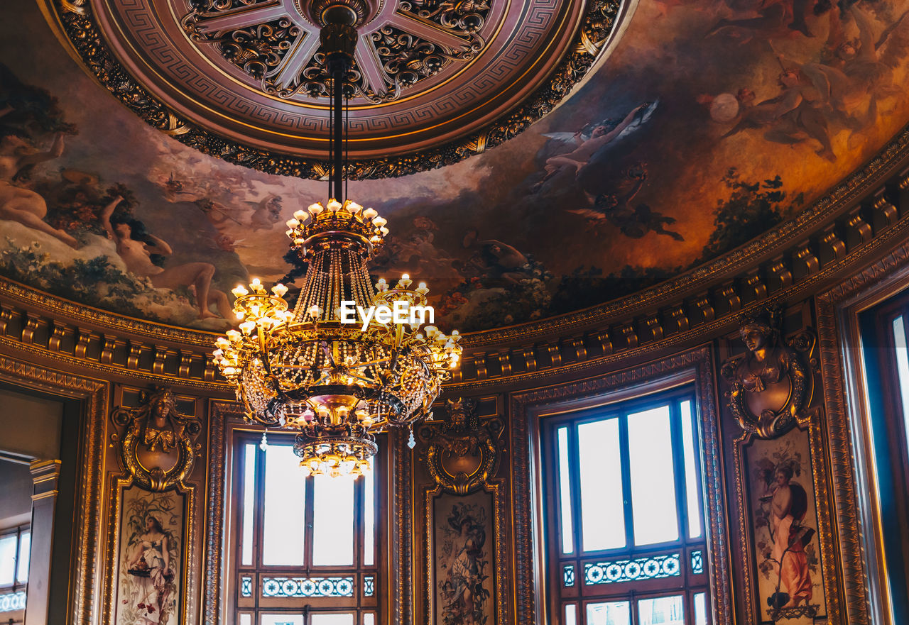 LOW ANGLE VIEW OF ILLUMINATED CHANDELIER HANGING ON CEILING OF BUILDING