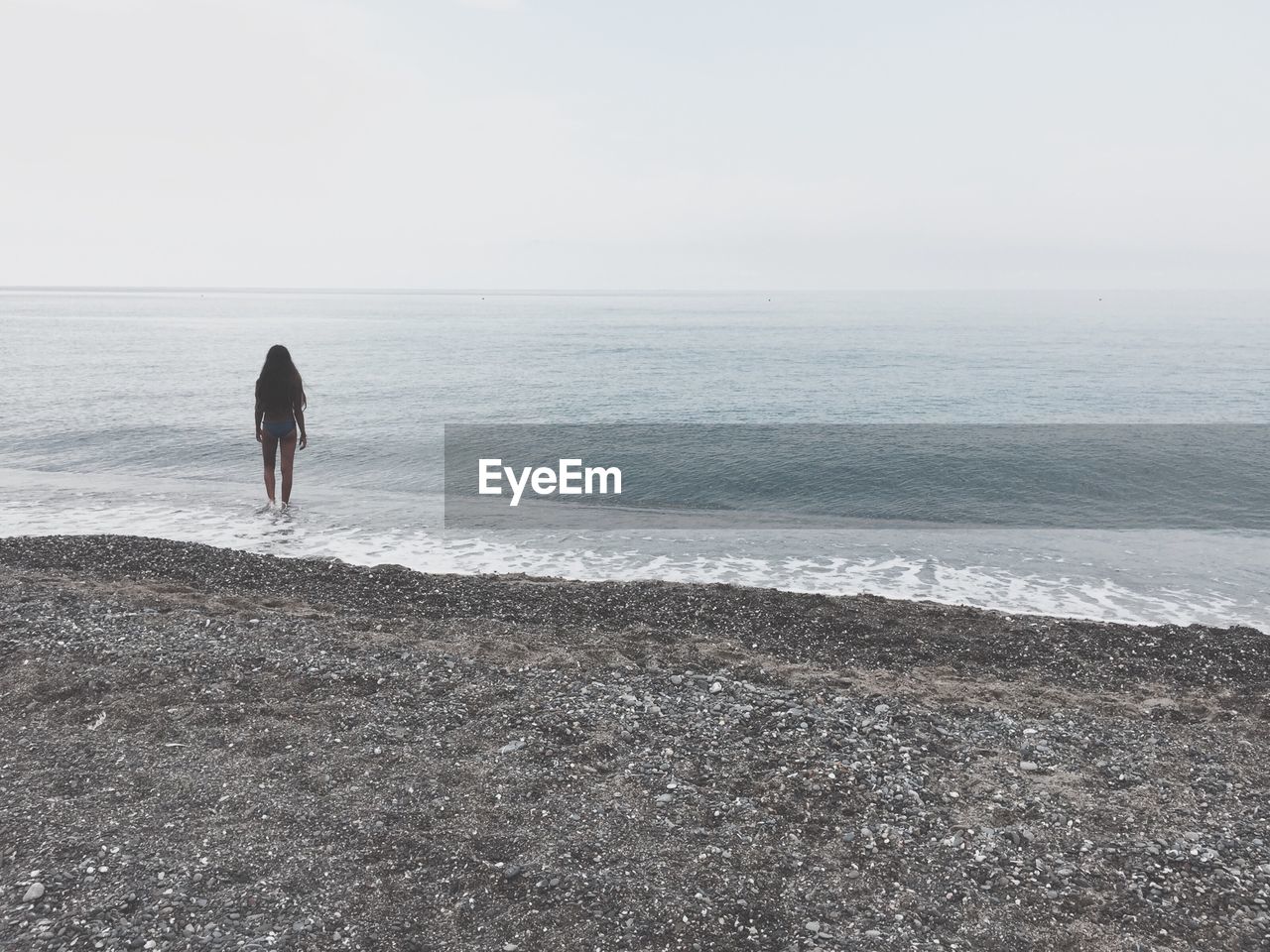 Rear view of woman walking on shore at beach against clear sky