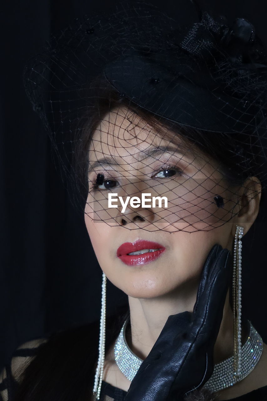 Close-up portrait of mature woman wearing veil against black background