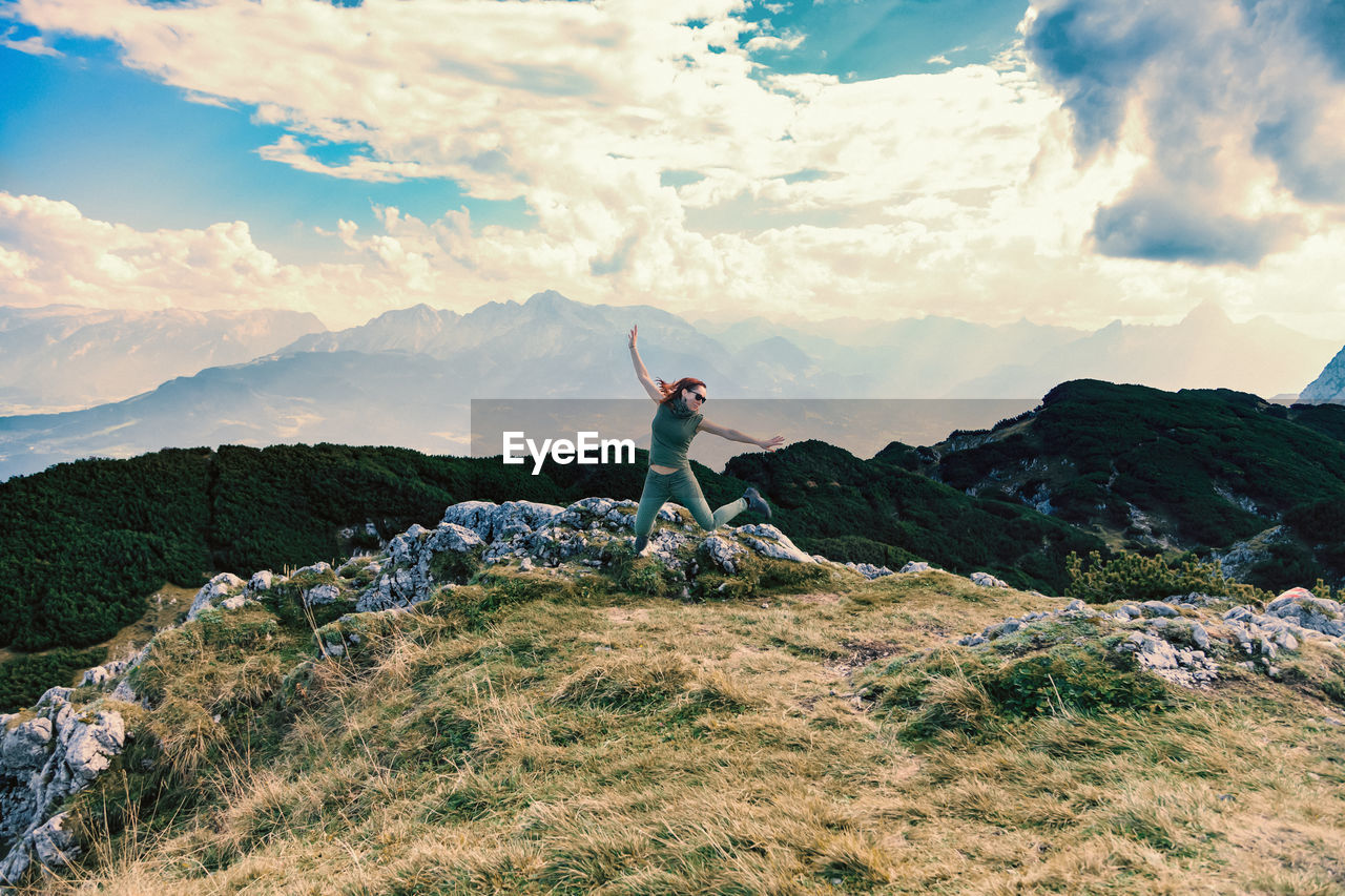 Happy woman jumping on mountain against cloudy sky