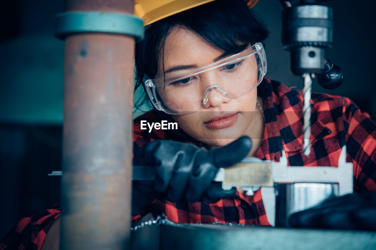 PORTRAIT OF YOUNG WOMAN WORKING IN METAL MACHINE