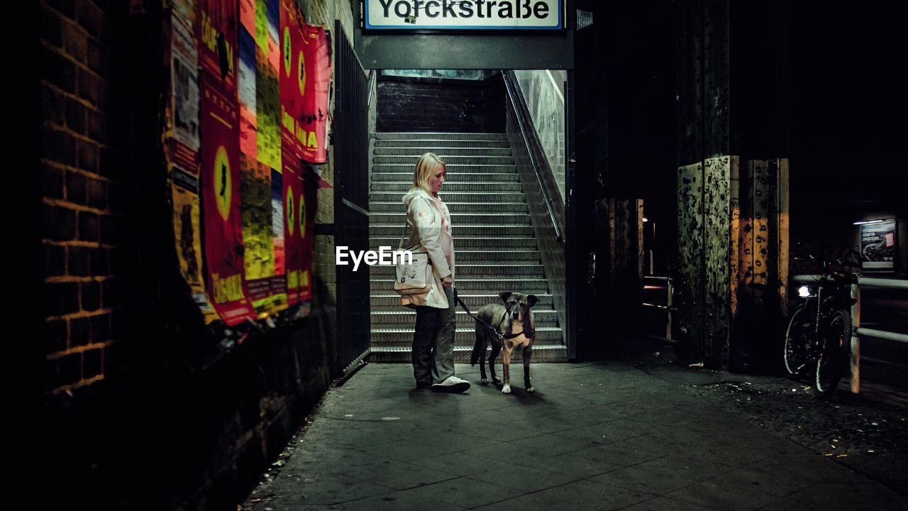 Full length of woman with dog standing on street at sunset