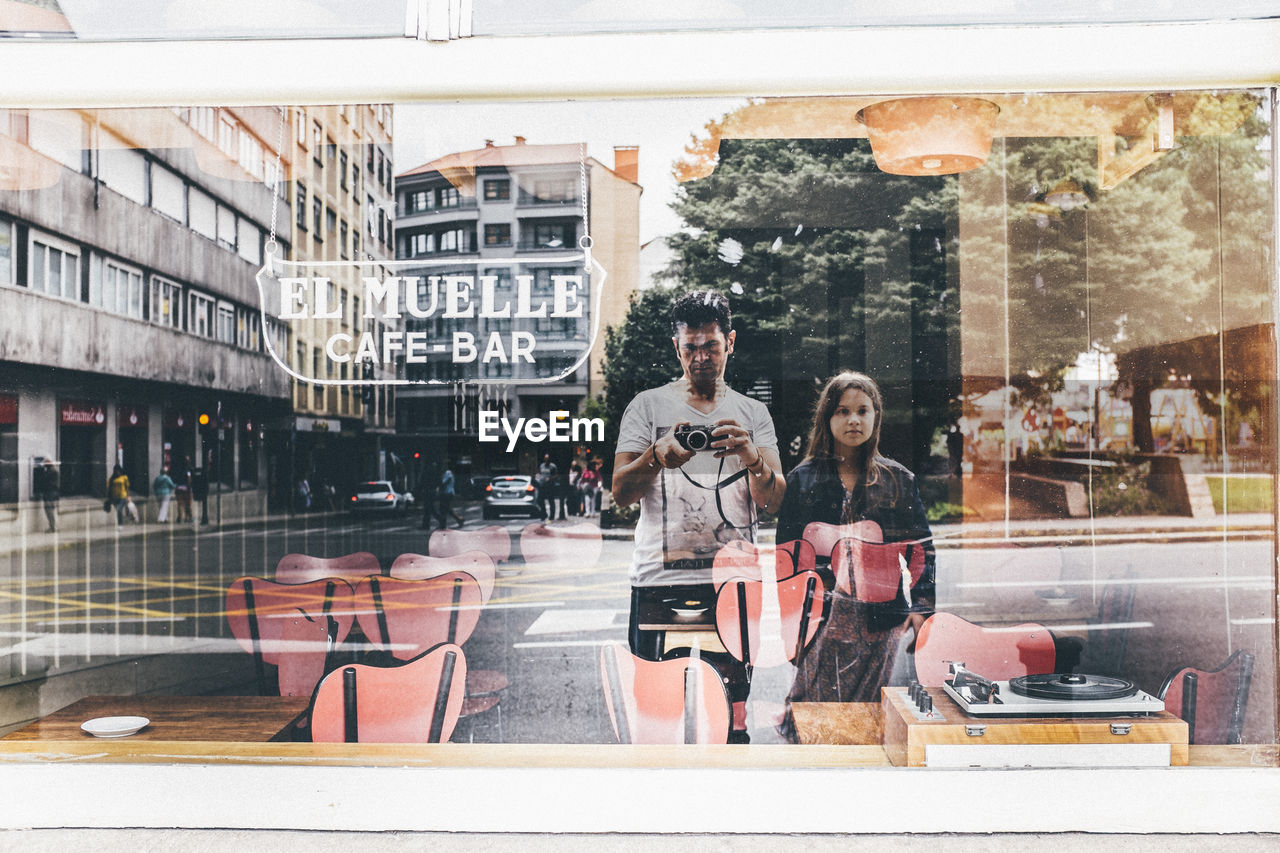 Man and woman with camera reflecting on glass window of restaurant