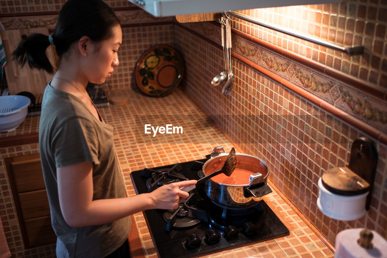 From above of female adding salt in saucepan while cooking marinara sauce from tomatoes on stove in kitchen