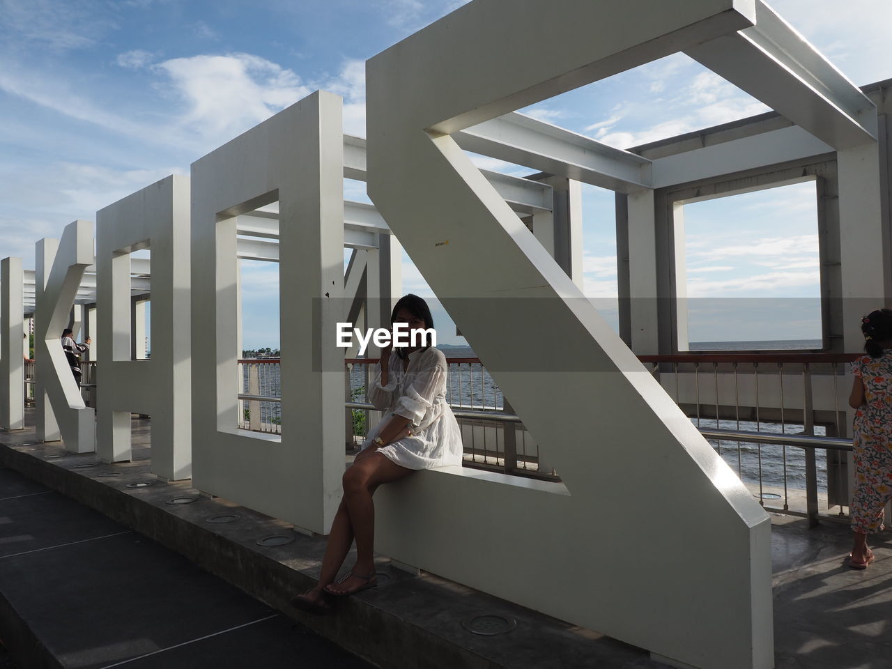 FULL LENGTH PORTRAIT OF YOUNG WOMAN SITTING ON BUILT STRUCTURE