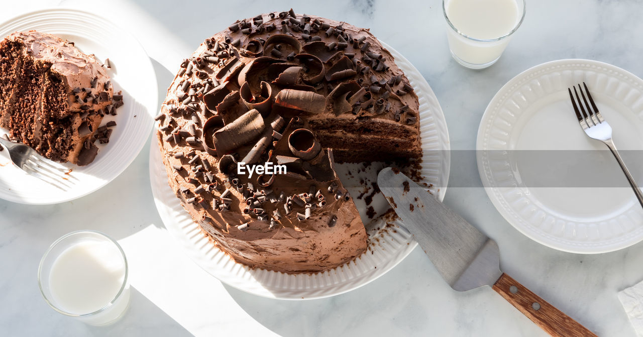 A chocolate cake decorated with chocolate curls with one slice to the left.