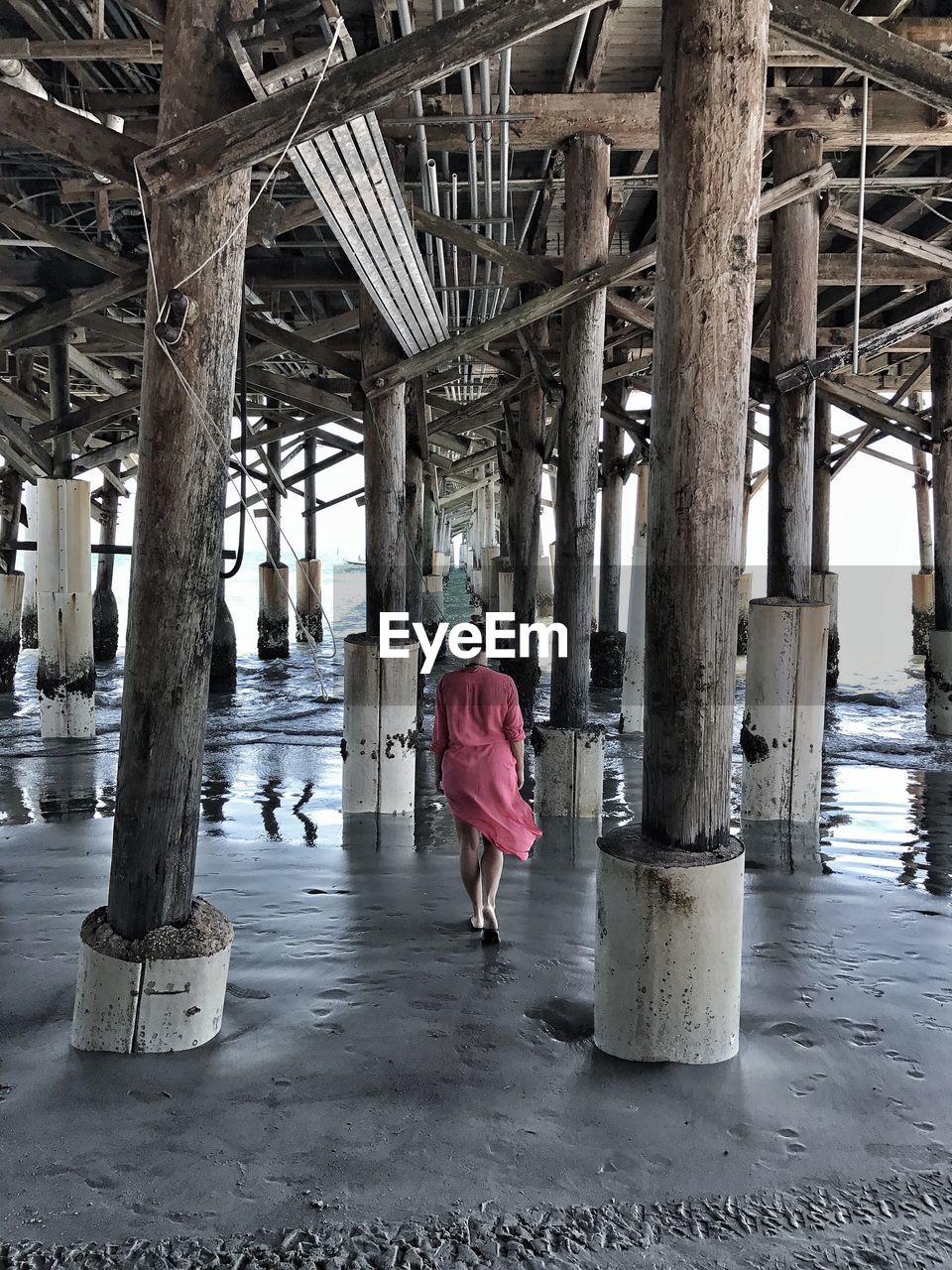 Rear view of a woman walking under pier at beach