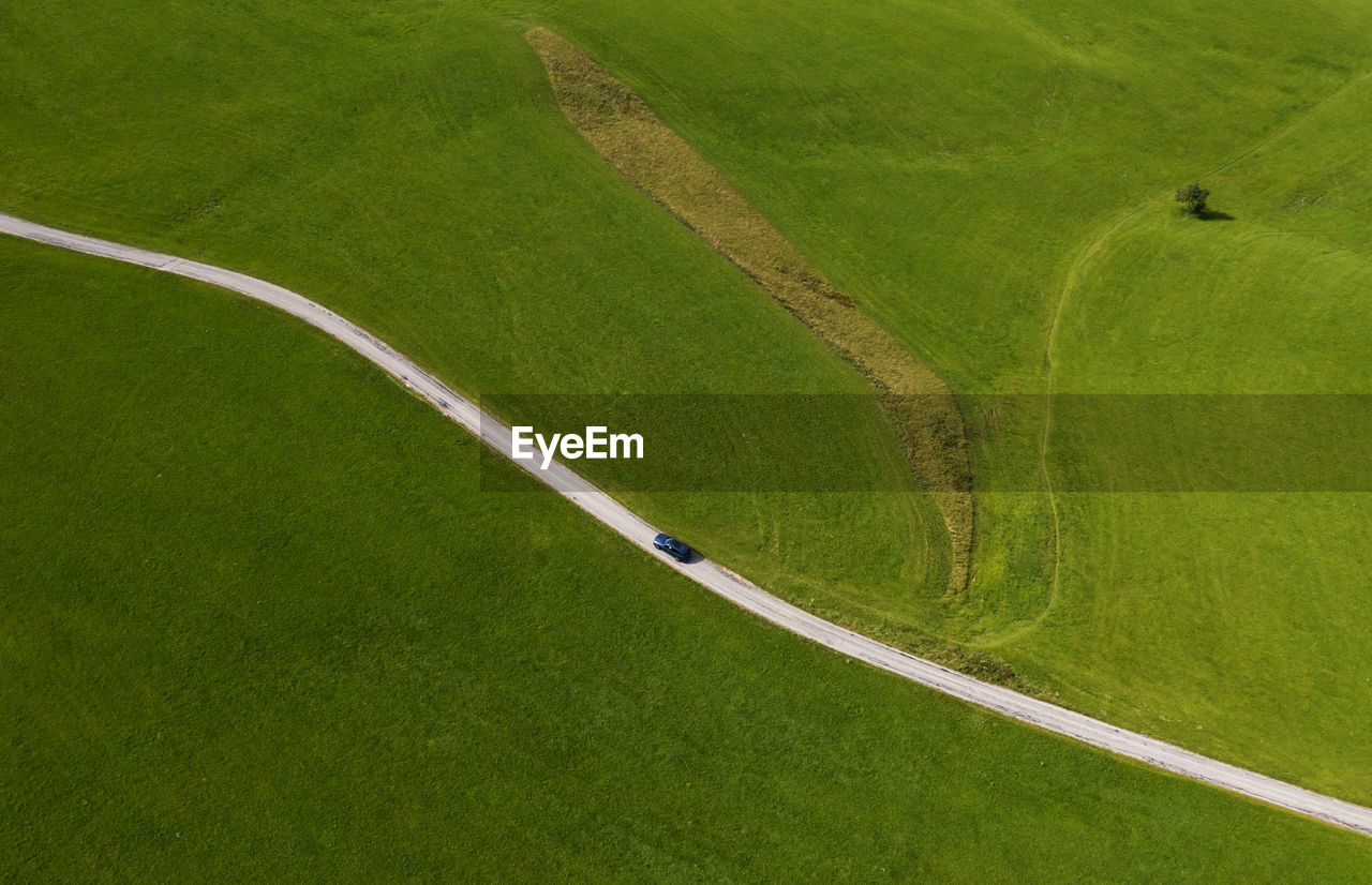 Austria, upper austria, hausruckviertel, drone view of car driving along dirt road cutting through green field