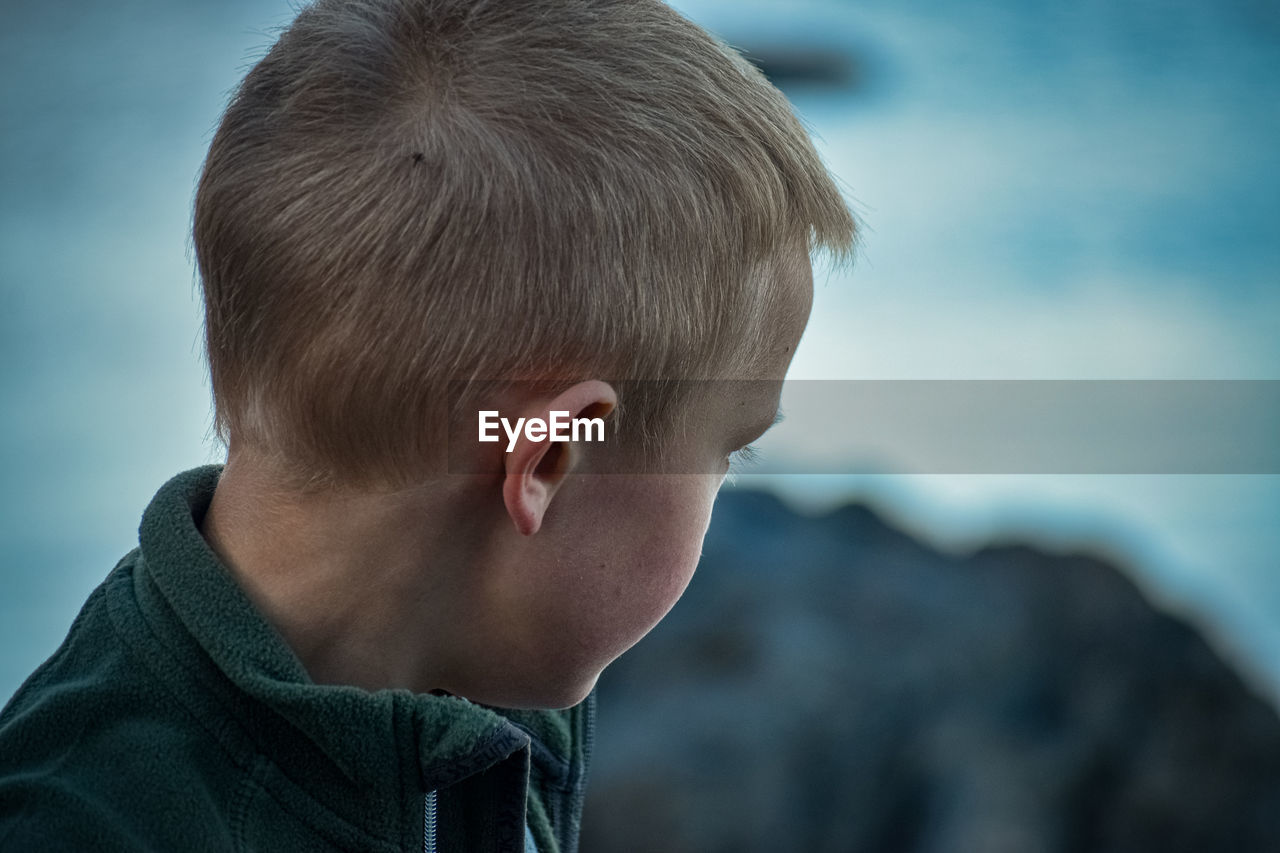 Close-up of boy looking away against sky