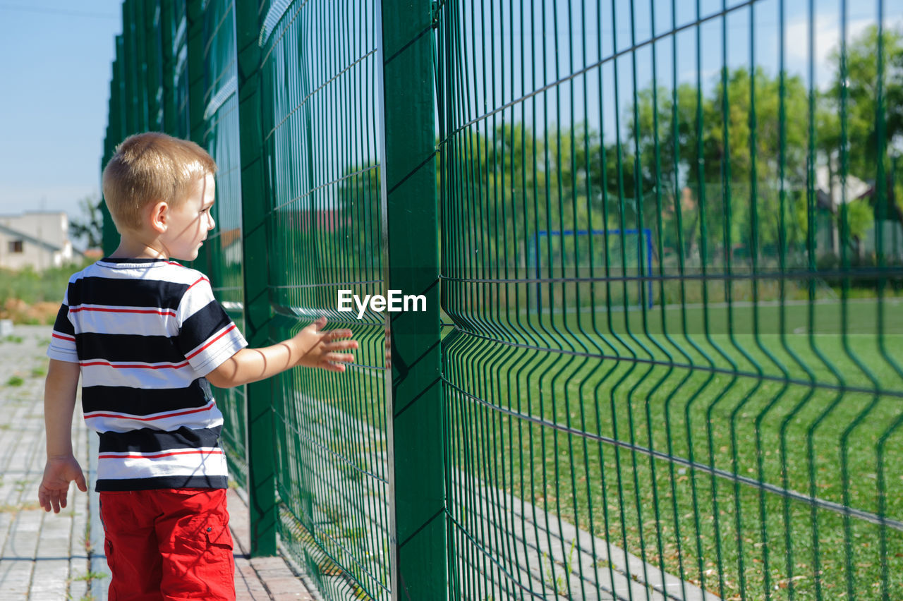 FULL LENGTH OF BOY LOOKING AT FENCE