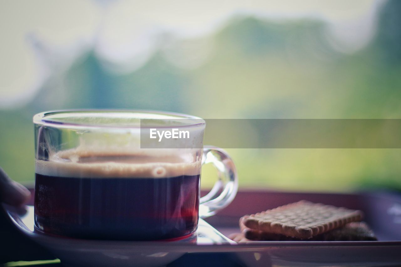 Close-up of coffee cup with cookies on table against window