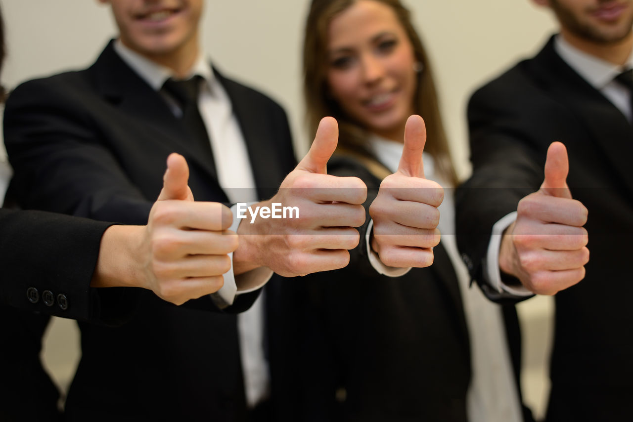 Midsection of business people showing thumbs up while standing in office