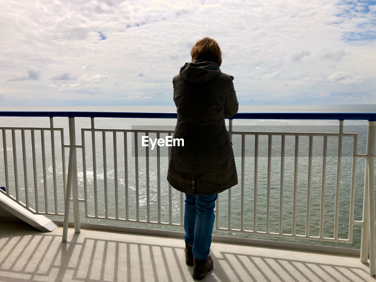 Rear view and silhouette of woman standing at the railing of a ship, gazing over the sea