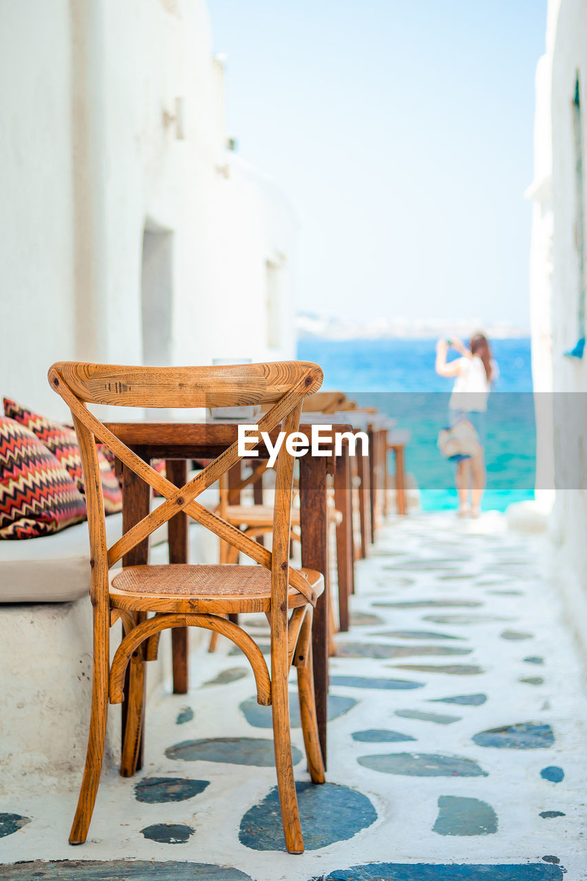 EMPTY CHAIRS AND TABLES ON BEACH AGAINST SKY