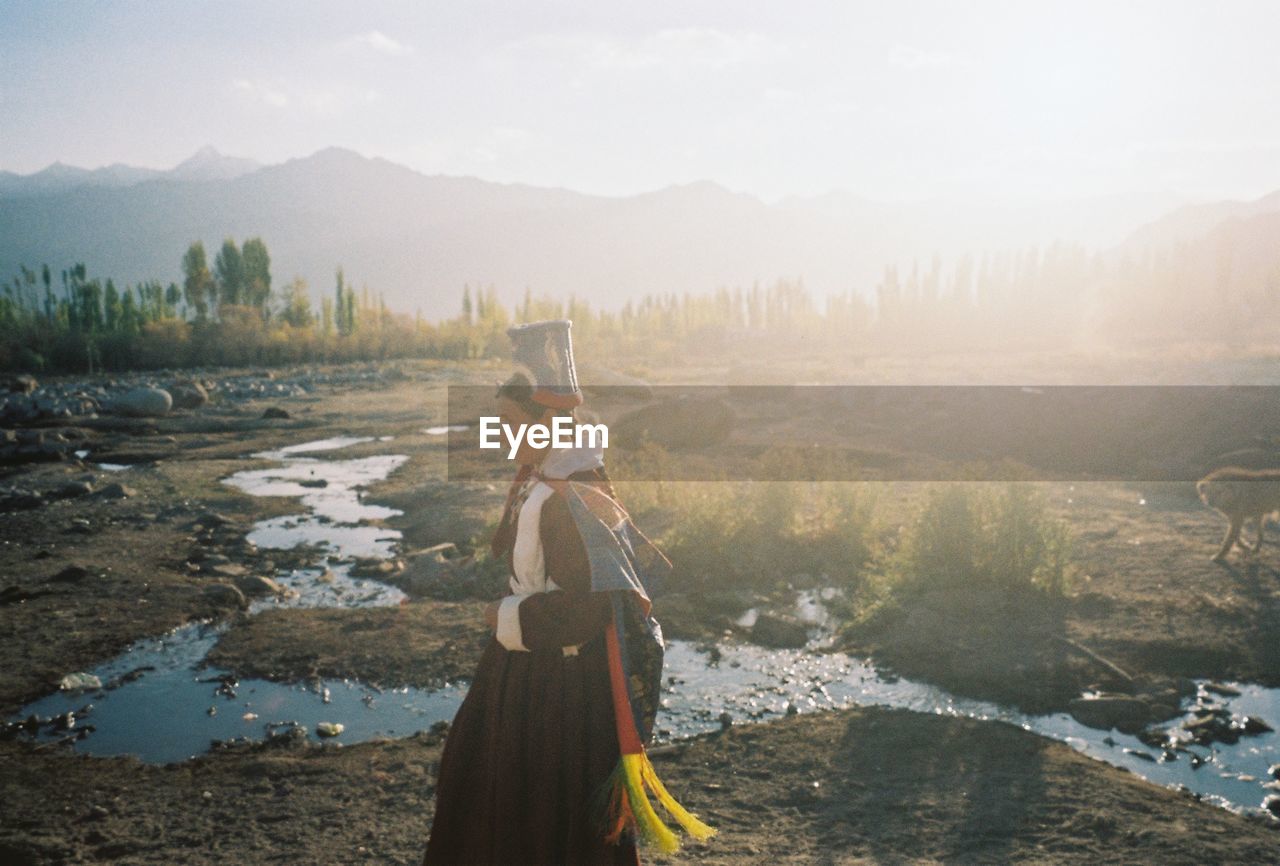 WOMAN STANDING ON RIVERBANK AGAINST SKY