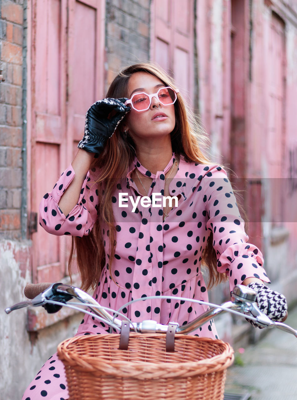 Portrait of model in pink dress and gloves on a bicycle in london