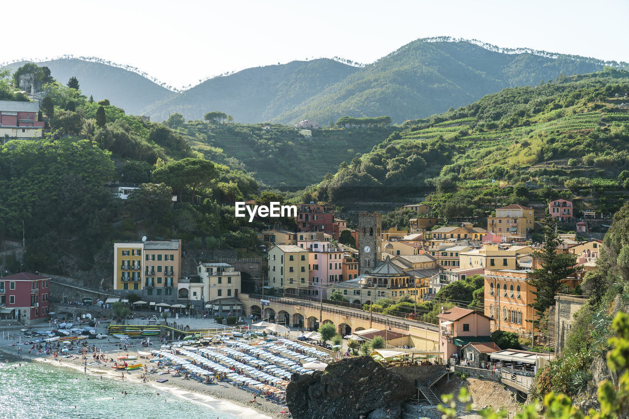 From above picturesque drone view of houses and beach of resort town located near sea against green mountains and sundown sky