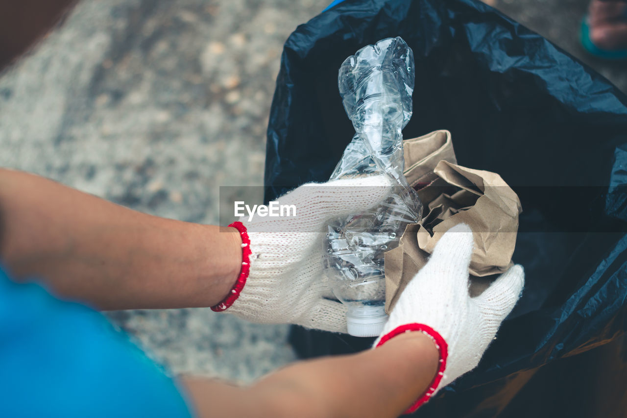 Cropped hands of person wearing gloves inserting garbage in plastic bag