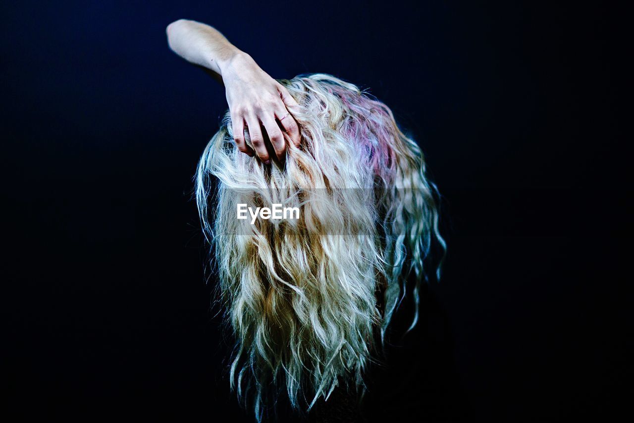 Digital composite image of hand holding blond hair against black background