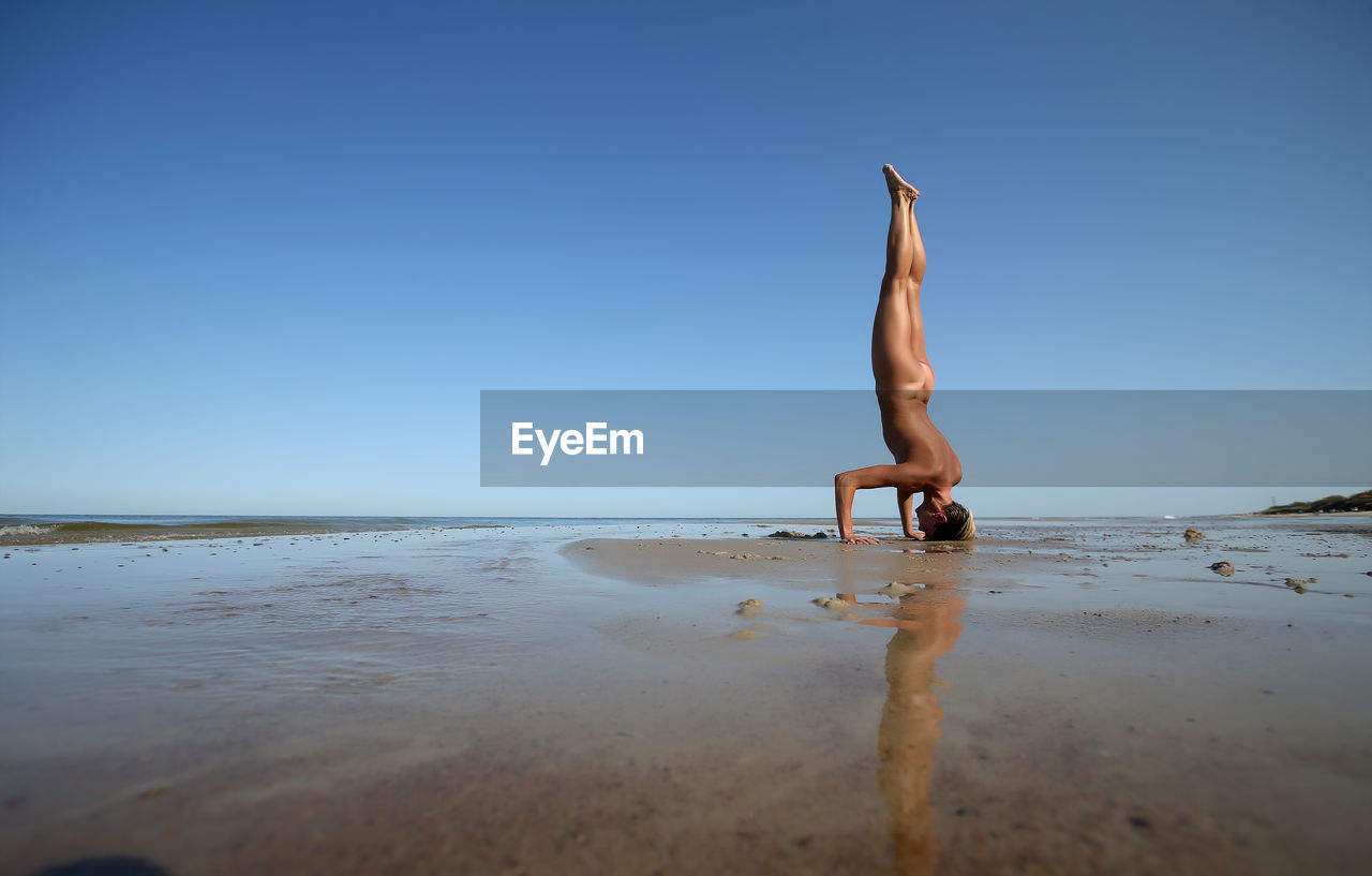 Naked woman doing handstand on beach against clear sky