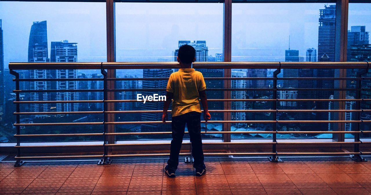 Rear view of boy looking at cityscape through glass window