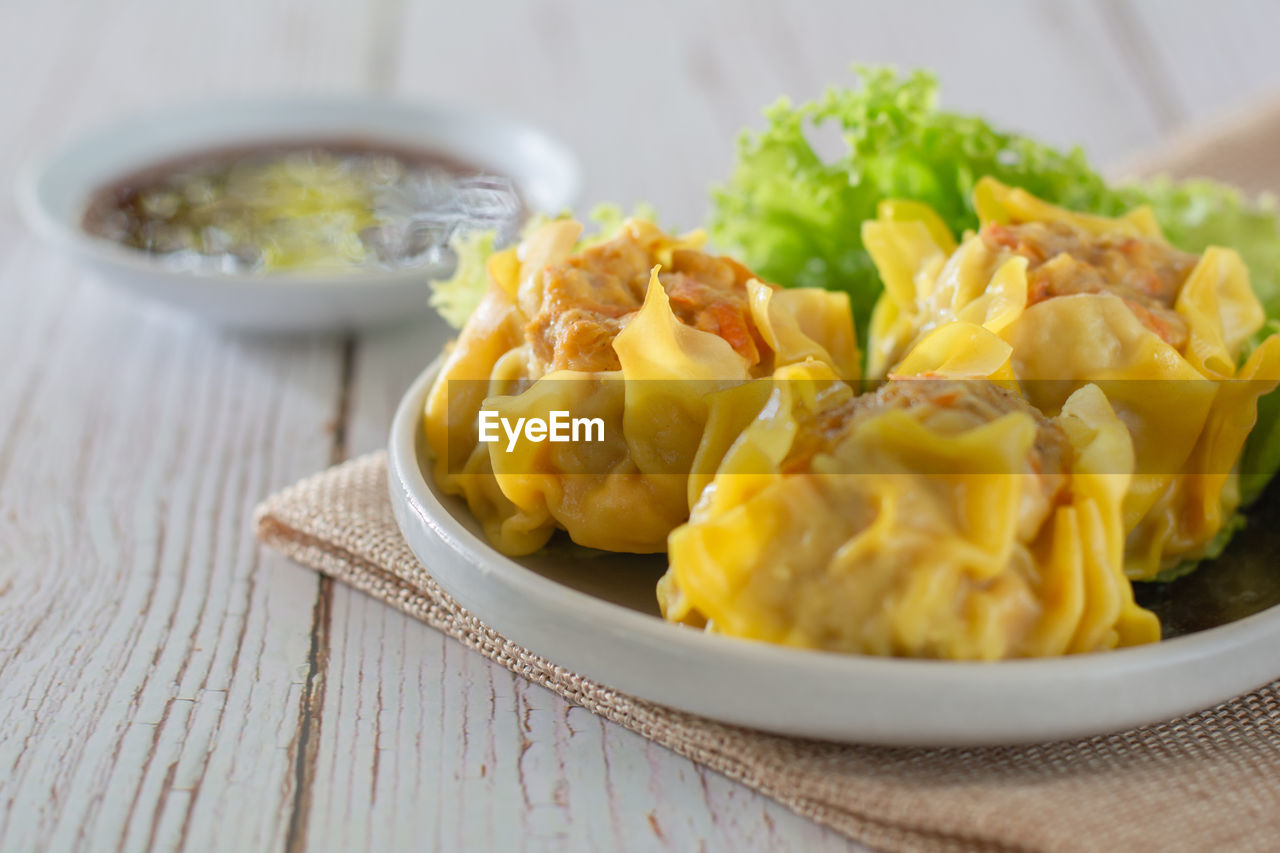 Chinese steamed dumpling, shumai on white dish served with soy sauce and lettuce leaves.