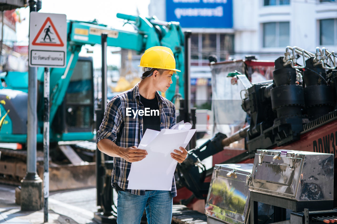 MAN WORKING ON PAPER AT CONSTRUCTION SITE AGAINST BLUE SKY