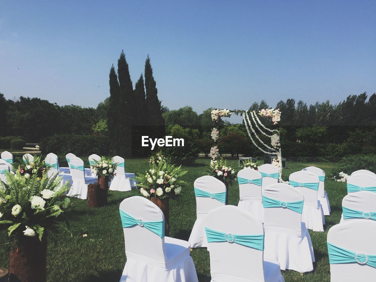 White chairs on grass during wedding reception against clear sky