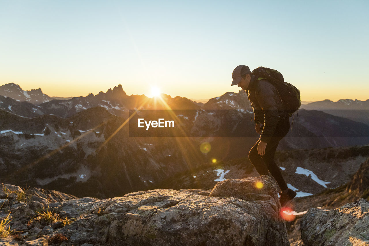 Backpacker scrambling over rocky terrain to reach mountain summit.